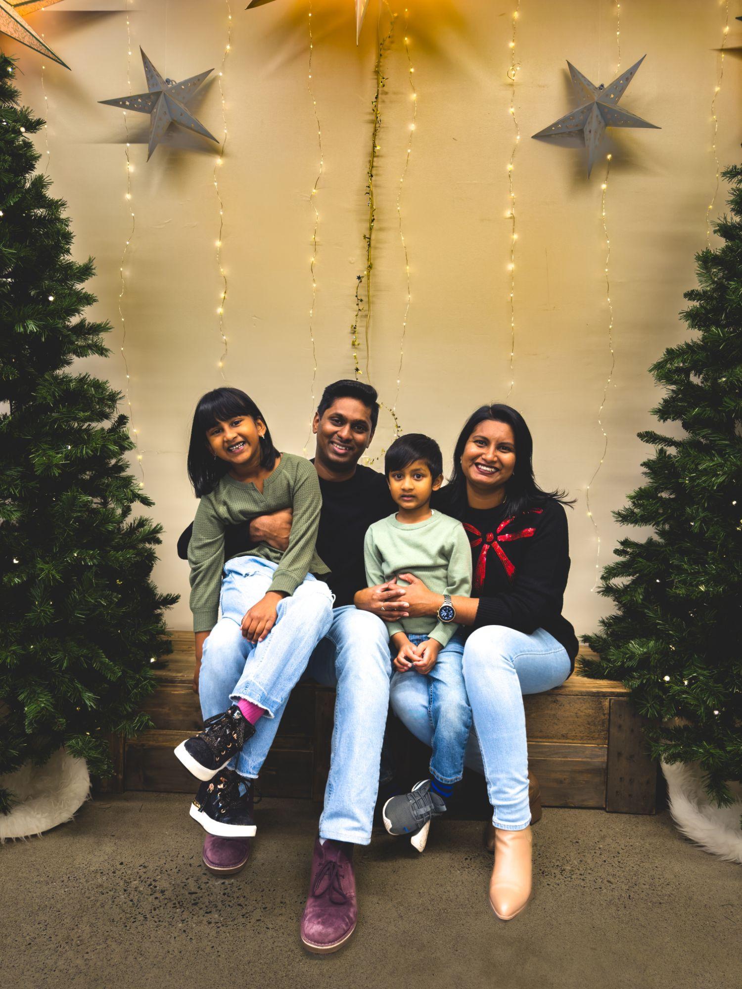Fredrick with his wife and their two children, seated on a bench between Christmas trees and paper stars.